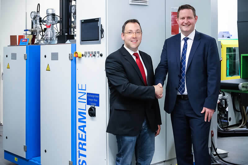 The new high-pressure metering machine STREAMLINE for the surface treatment of plastic moulded parts with the two engineers responsible for the surface project, Mr. Dominik Malecha from the Plastics Institute for SMEs (K.I.M.W.) in Lüdenscheid and Mr. Alexander Frank, Hennecke GmbH (from left to right)